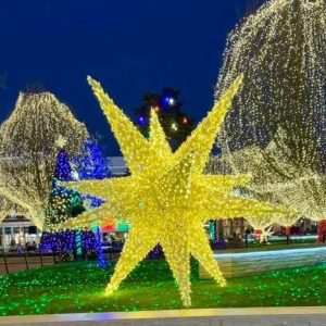 Large illuminated starburst sculpture anchoring a public lawn at dusk