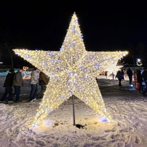 Illuminated hollow star sculpture installed on a snowy downtown plaza
