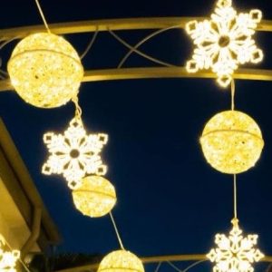 Hanging fiberglass orbs and snowflake pendants forming a lit canopy over a walkway